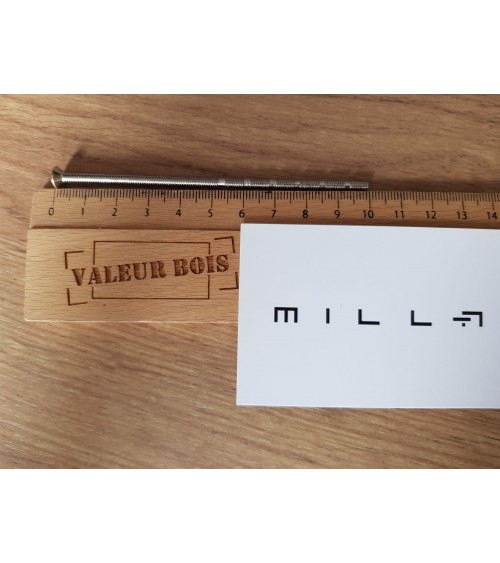Varilla roscada pasante M4 de 10cm de longitud sobre una mesa, con una regla de madera y tarjeta de visita blanca millapoignees