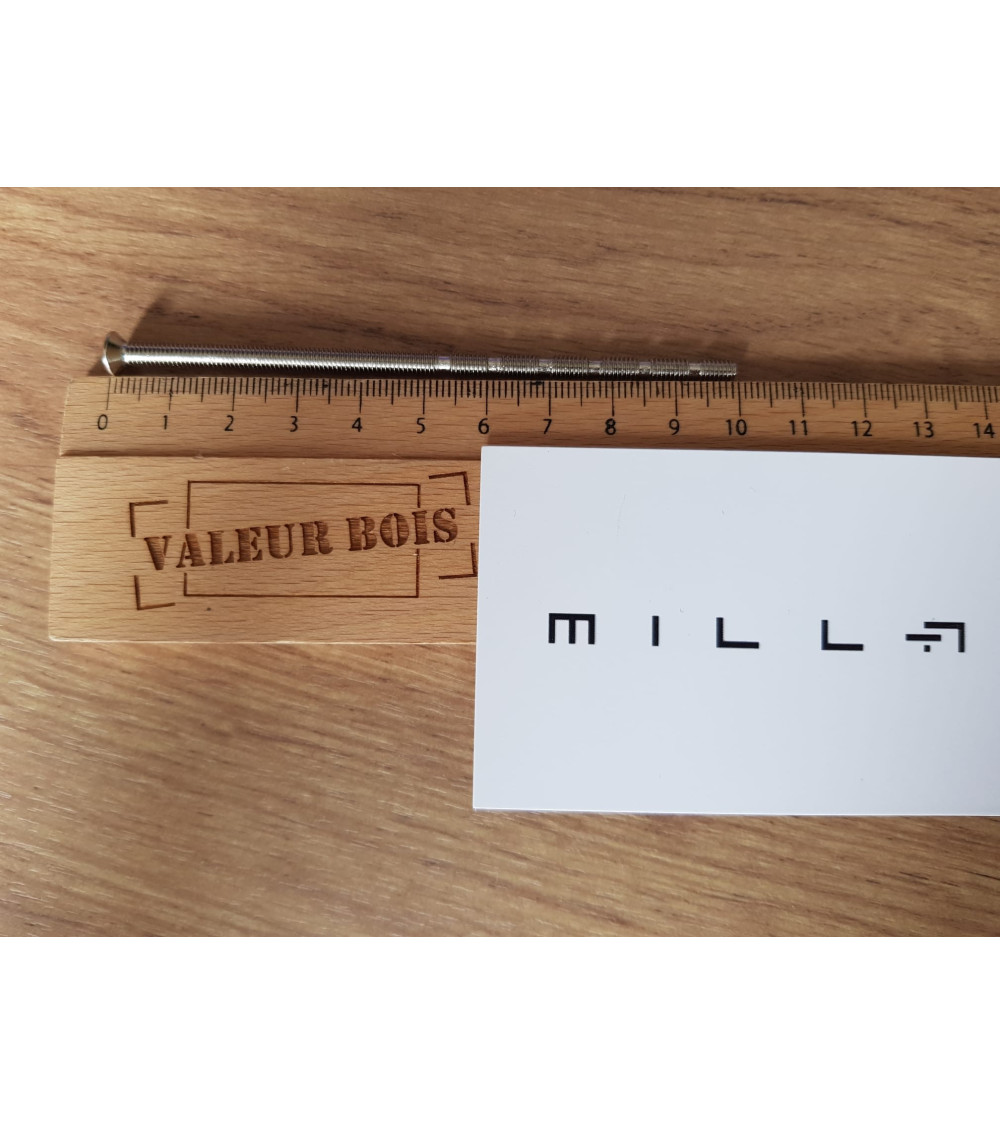 Varilla roscada pasante M4 de 10cm de longitud sobre una mesa, con una regla de madera y tarjeta de visita blanca millapoignees