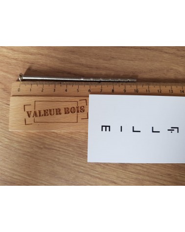 Varilla roscada pasante M4 de 10cm de longitud sobre una mesa, con una regla de madera y tarjeta de visita blanca millapoignees