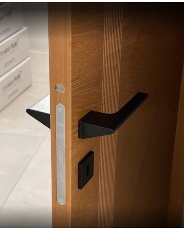 Tirador de puerta negra LUPINA de diseño montado en una puerta entreabierta
