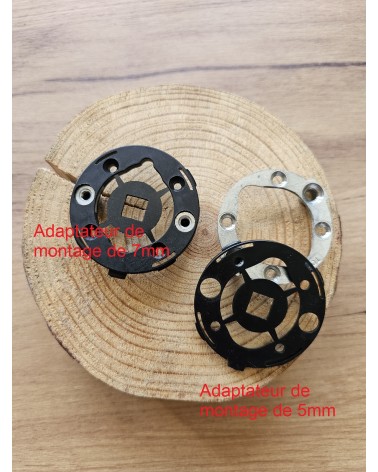 Dos adaptadores de montaje rápido para tiradores de puerta vistos de frente, apoyados sobre una mesa de madera