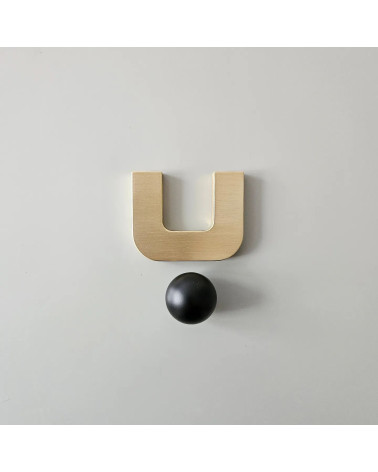 Tirador de mueble en oro pulido ISA XS tirador de diseño con una esfera negra visto de frente sobre una superficie clara