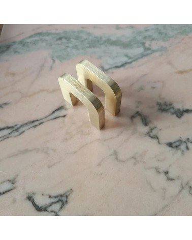 Tirador de mueble en oro pulido ISA XS tirador de diseño visto en perspectiva diagonal colocado plano sobre una superficie de má