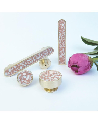 Tirador de mueble en latón y Pink Terrazzo tirador de diseño colocado junto a una flor sobre fondo blanco