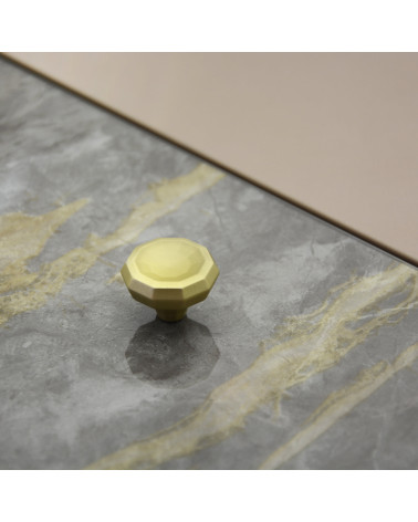 Tirador de mueble oro mate CAMPANA asa de diseño colocado sobre una superficie plana con fondo texturizado